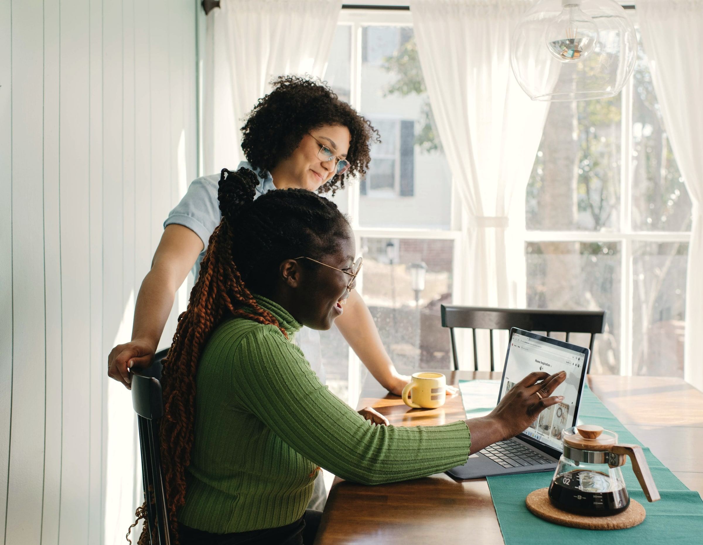 Two people review plans together at a sunlit table with a laptop and coffee.