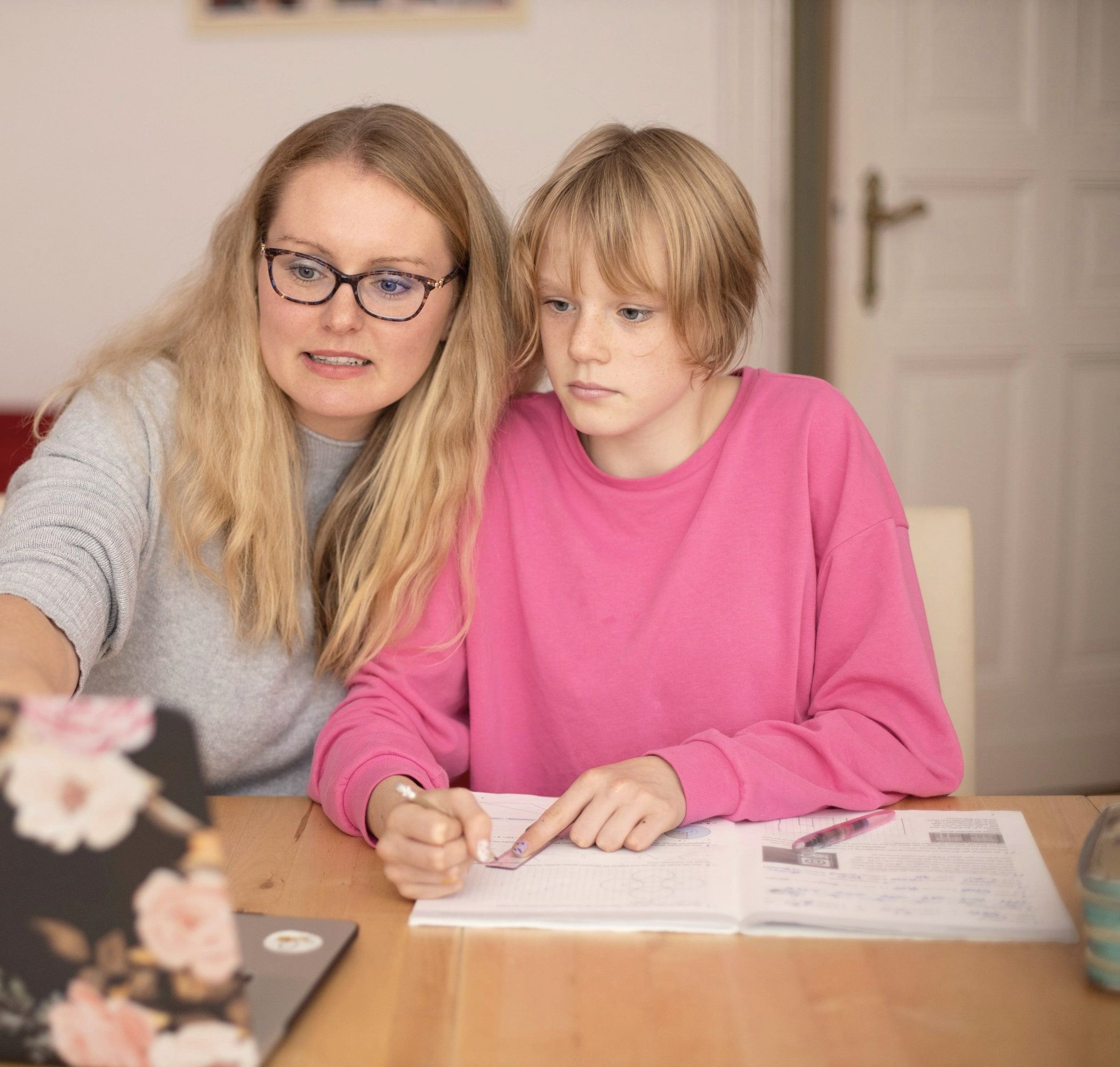 A parent and a teenage student look at a laptop together while the student takes notes.